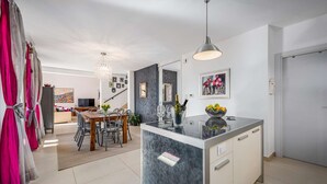 A modern kitchen with a marble island, a dining area with a wooden table, and a living room with a sofa and TV. - Villa Clariss (Visnjan)