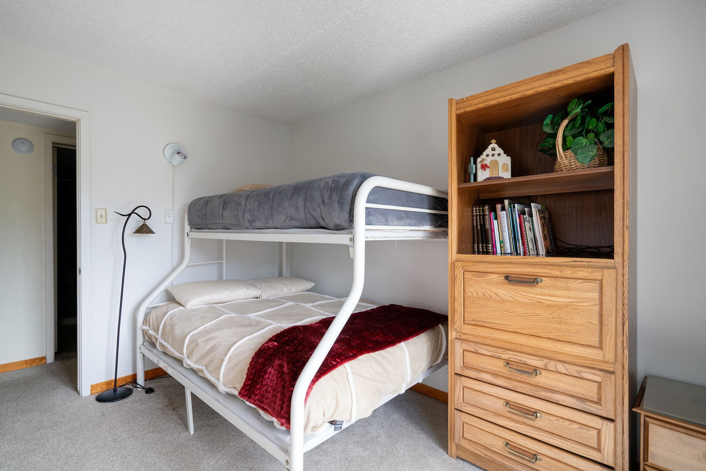 A bunk bed with a wooden dresser and a bookshelf.