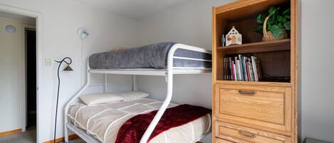 A bunk bed with a wooden dresser and a bookshelf.