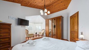 A hotel room with a large bed, wooden wardrobe, a television, and a seating area with chairs and a table. - Villa Eufemia (Porec)