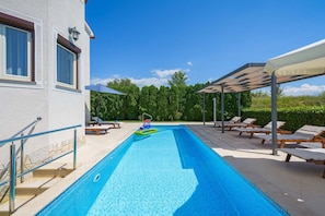 Una piscina con tabla de salto, sillas de descanso y una pérgola.