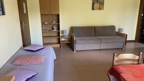 Una habitación con dos camas individuales, un sofá, un armario de madera y una pequeña mesa con una lámpara.