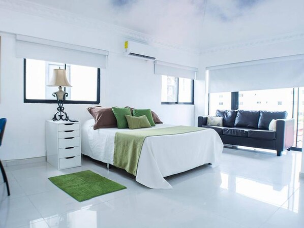 Relax in a serene space with a neatly made bed, white dresser, and comfortable sofa.