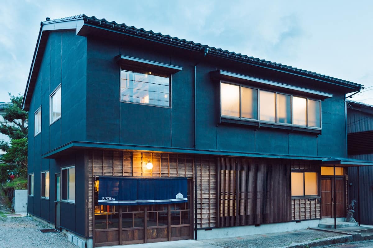 A modern two-story building with a dark facade, large windows, and a visible storefront with a blue awning.