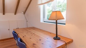 Una mesa de madera con una lámpara, una silla y un ventanal con vistas a árboles.