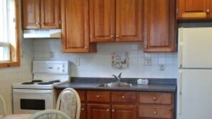 A kitchen with wooden cabinets, a refrigerator, a stove, and a dining table with chairs. - Suites of Wasaga Beach Area 2- mins walk Beach 1 (Wasaga Beach)