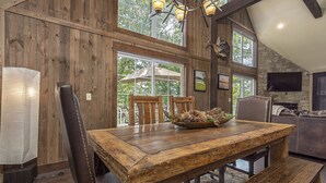 Un coin repas rustique avec une table et des chaises en bois, une cheminée en pierre et de grandes fenêtres donnant sur l’extérieur.