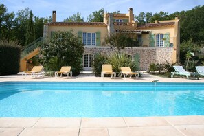 Ein Pool mit Liegestühlen, ein Steinhaus mit Ziegeldach und eine Treppe, die zu einem Balkon führt.