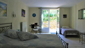Un dormitorio con una cama grande, una cama más pequeña, un escritorio y una silla. Hay una ventana con vista a follaje exterior.