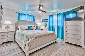 Een slaapkamer met een groot bed, een plafondventilator, een televisie en een dressoir.