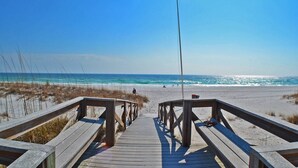 Ein hölzerner Steg führt zu einem Strand bei blauem Himmel.