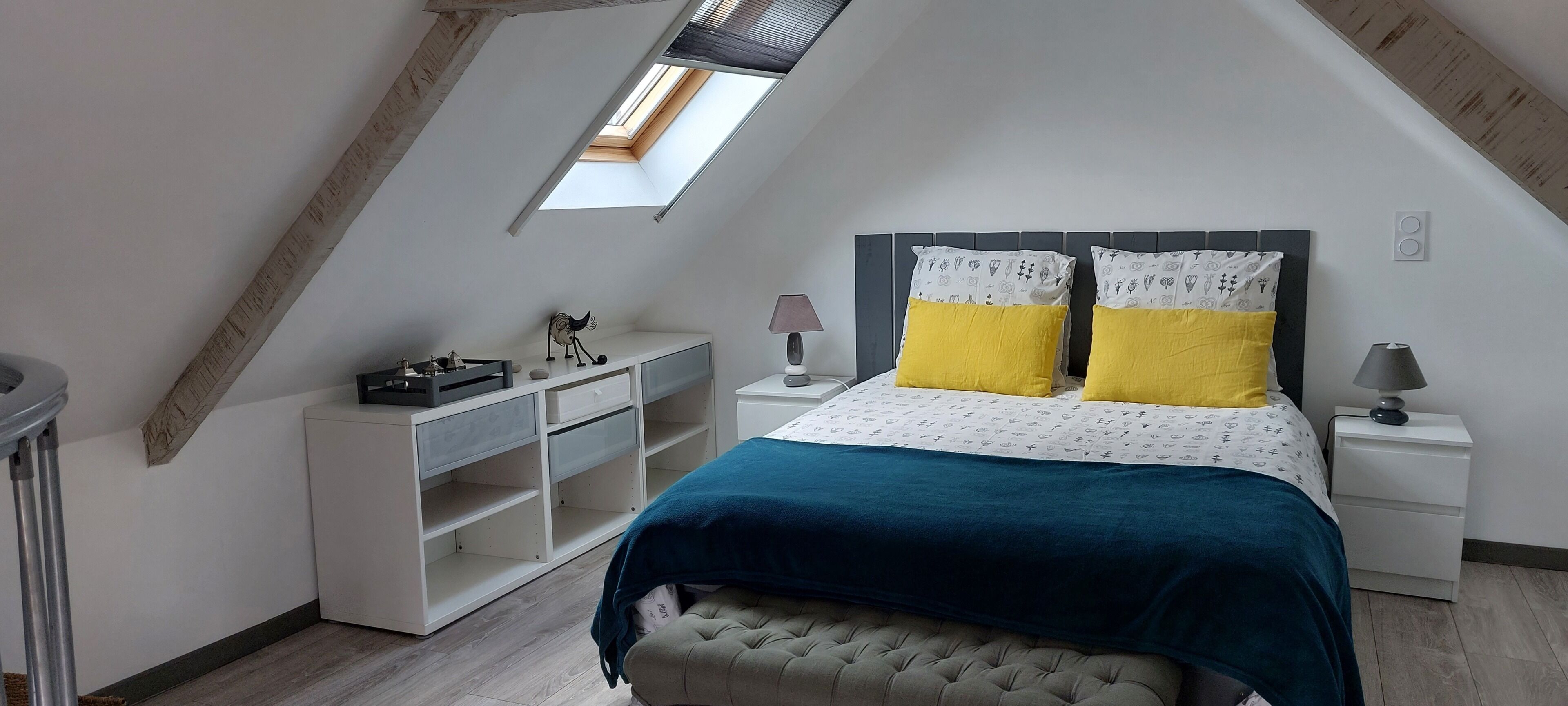 A bedroom with a sloped ceiling, a skylight, a bed with patterned pillows, bedside tables, and a storage unit.