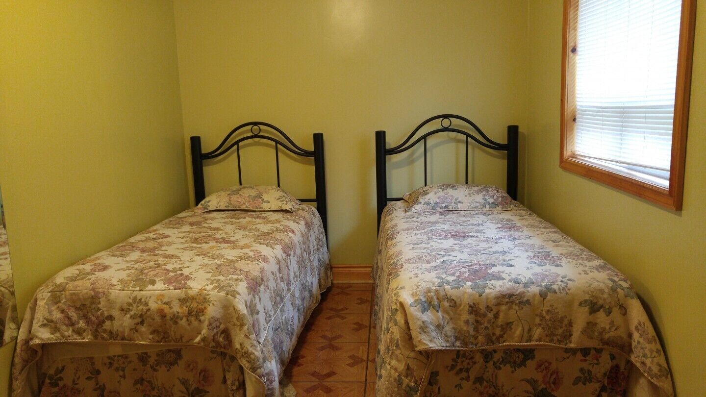 Una habitación pequeña con dos camas individuales, cada una con una colcha estampada de flores, frente a paredes amarillas.