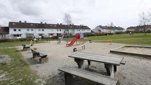 Un parque infantil con tobogán y columpios, rodeado de un parque con mesas de picnic y bancos.