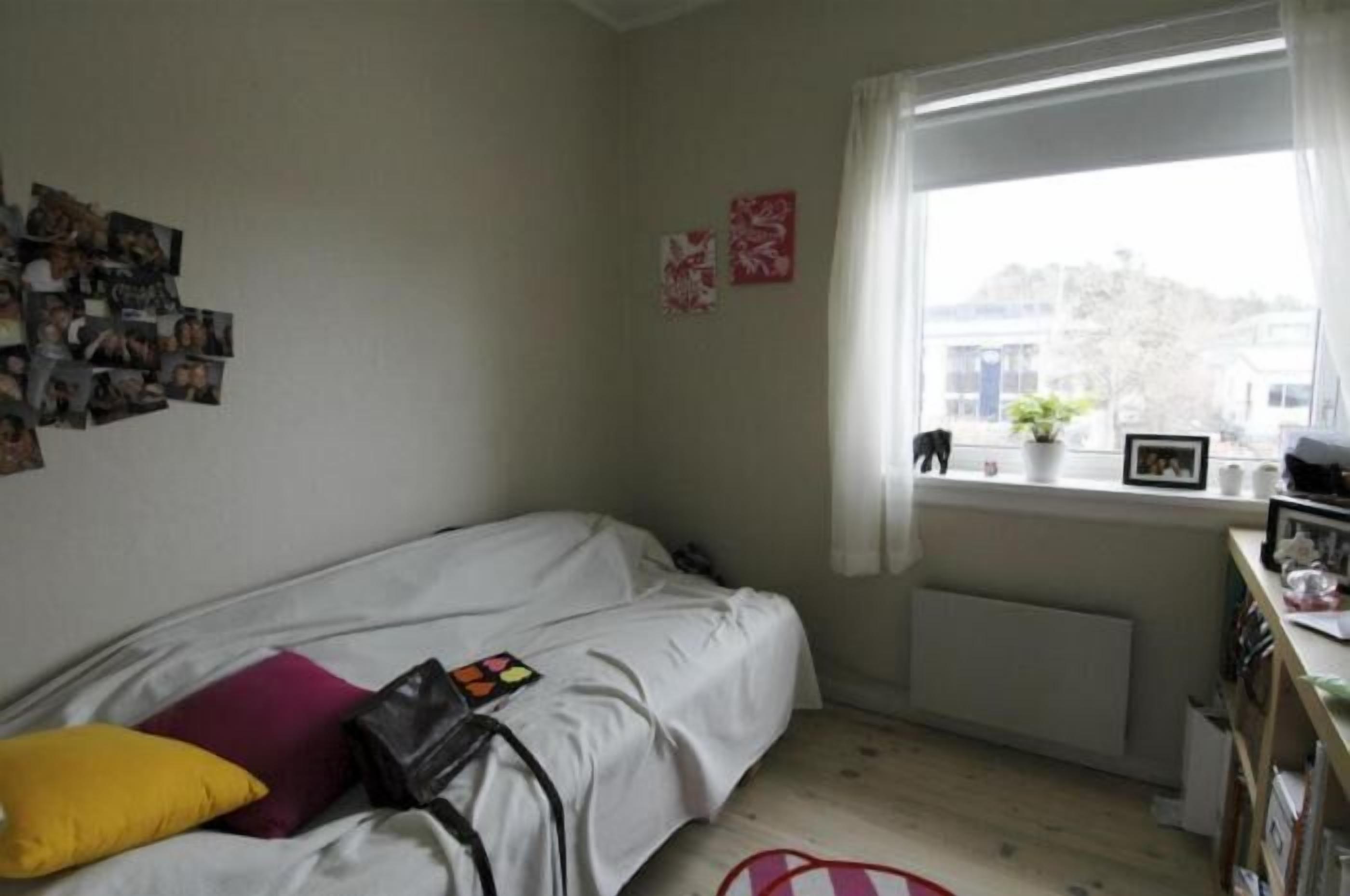 A bedroom with a bed, a window with a view, and a wall with photos.