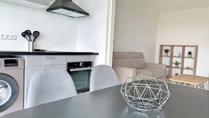 A modern kitchen with a built-in oven, a dining table with a geometric centerpiece, and a sofa in the living area. - Apparemment F2 vue mer (Les Trois-Îlets)