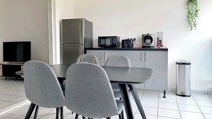 A modern kitchen with a dining area, including a TV, refrigerator, microwave, and a hanging plant. - Apparemment F2 vue mer (Les Trois-Îlets)