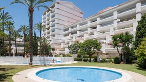 Un hotel con una piscina grande rodeada de palmeras y un edificio de varios pisos con balcones.