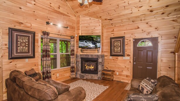 A cozy log cabin interior with a fireplace, leather sofas, and a television.