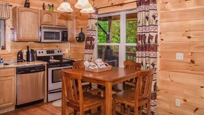 A wooden cabin kitchen with wooden cabinets, a microwave, an oven, a dishwasher, and a dining table with chairs.