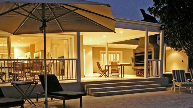 A poolside area with a wooden deck, lounge chairs, and an umbrella. - Kowie River Guest House (Port Alfred)