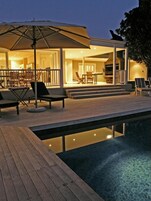 Un área junto a la piscina con cubierta de madera, sillas de descanso y una sombrilla.