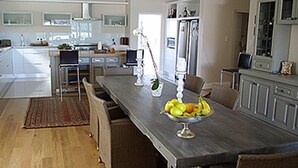A modern kitchen with a long dining table, a chandelier, and a fruit bowl. - Kowie River Guest House (Port Alfred)