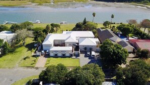 A large, multi-story house with a spacious front yard, a swimming pool, and a view of a lake. - Kowie River Guest House (Port Alfred)