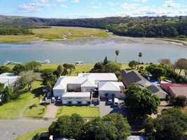 Una casa grande de varios pisos con un amplio jardín delantero, piscina y vista a un lago.