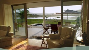 A spacious room with a large sliding glass door leading to an outdoor patio with a pool, chairs, and a table. - Kowie River Guest House (Port Alfred)