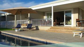 Uma área na piscina com espreguiçadeiras, guarda-sol e um alpendre coberto.