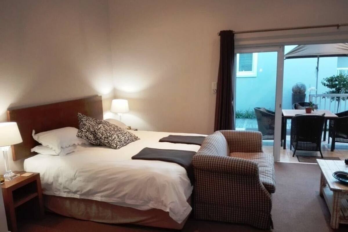 Ein Hotelzimmer mit Bett, Stuhl, Tisch und Blick ins Freie.