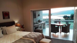A hotel room with a bed, a small table, and a balcony with a view of the water. - Kowie River Guest House (Port Alfred)