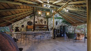 A rustic outdoor bar area with stone walls, wooden beams, and a thatched roof.