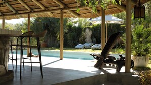 Un espacio al aire libre techado con piscina, sillas de descanso y una estatua.