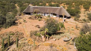 A thatched-roof building with multiple rooms, surrounded by a dry, rocky landscape with sparse vegetation.