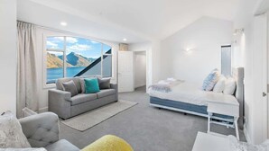 A modern bedroom with a large window, a sofa, a bed, and a small table. - Million Dollar Views | Central Luxury | Private Hot Tub (Queenstown)