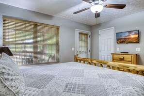 A bedroom with a bed, wooden headboard, two windows with blinds, a ceiling fan, a TV on the wall, and a dresser. - Pigeon Forge One story 3 bedroom Creekside-Enjoy the sounds of the creek- Seasonal Pool Access (Pigeon Forge)