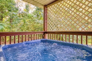 Un jacuzzi en una terraza de madera con un fondo de celosía, rodeado de vegetación exuberante.