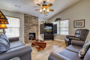 A living room with a stone fireplace, a ceiling fan, a television, and leather furniture. - Pigeon Forge One story 3 bedroom Creekside-Enjoy the sounds of the creek- Seasonal Pool Access (Pigeon Forge)