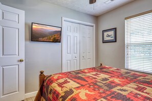 Um quarto com cama, porta, quadro emoldurado e janela com persianas.