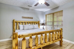 A bedroom with a wooden bed, a ceiling fan, a window with blinds, and a wall-mounted sign.