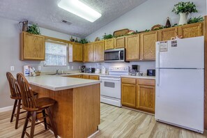 Una cocina con armarios de madera, una isla central con taburetes de bar, un microondas, una estufa y un refrigerador.