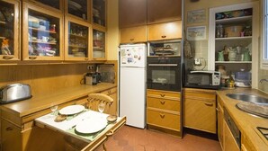 A compact kitchen with wooden cabinets, a refrigerator, an oven, a microwave, and a dining area with a table set for two.