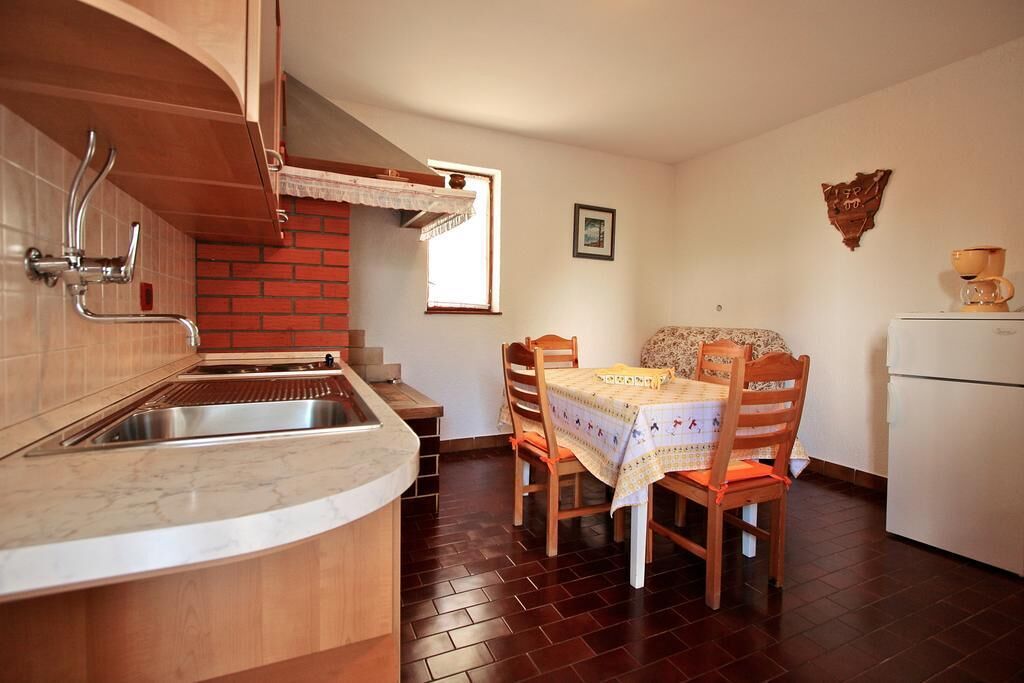 A kitchen with a sink, wooden cabinets, a dining table with chairs, a refrigerator, and a window.