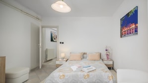 Un dormitorio con cama, mesitas de noche, un sillón, un radiador y un cuadro en la pared.