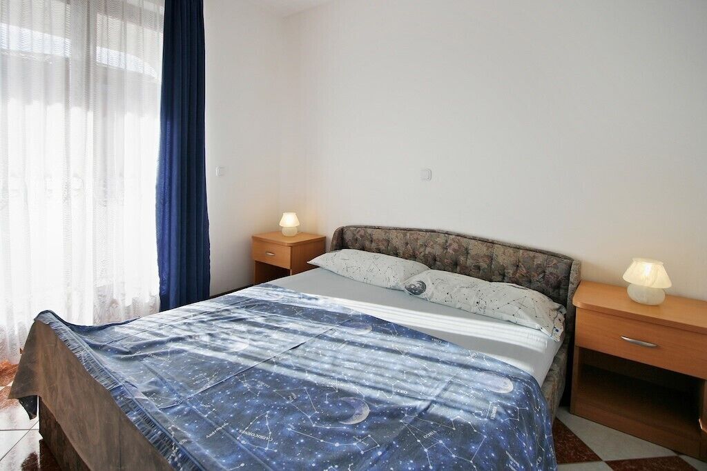Ein Schlafzimmer mit einem Bett, zwei Nachttischen, einem Fenster mit Vorhängen und einer Steckdose.