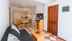 A compact living space with a sofa, a coffee table, a TV, a kitchen area, and a wooden door.