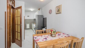 Un coin repas avec une table et des chaises en bois, un panier de fleurs et une cuisine en arrière-plan.