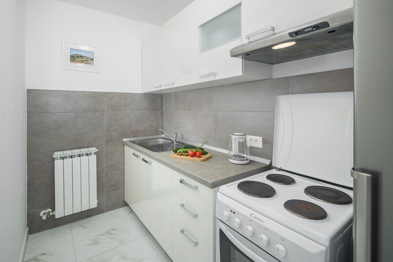 Eine moderne Küche mit weißen Schränken, einem Gasherd, einem eingebauten Backofen, einer Spüle und einem Wasserkocher auf der Arbeitsplatte.